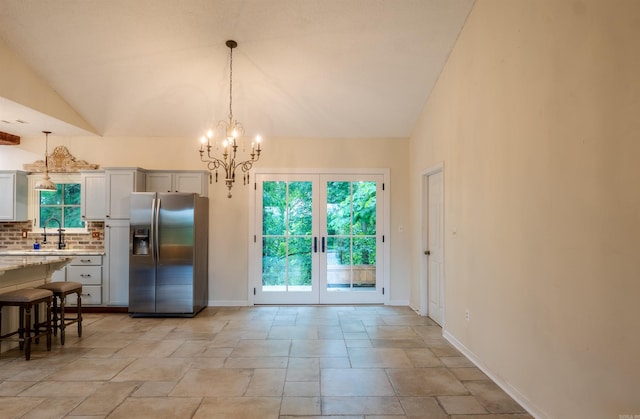 dining space featuring french doors, lofted ceiling, a chandelier, light stone finish flooring, and baseboards
