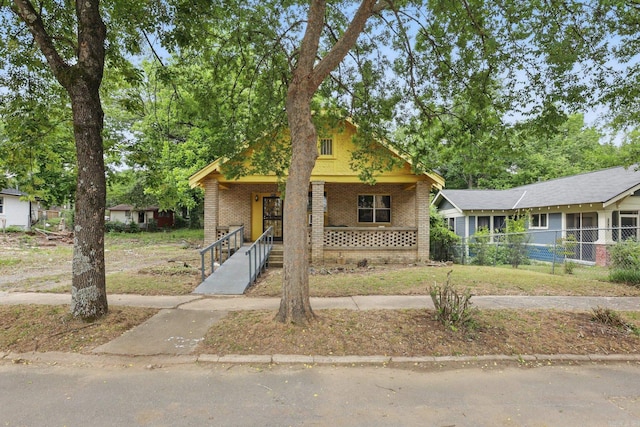 view of front of property featuring covered porch, brick siding, and fence