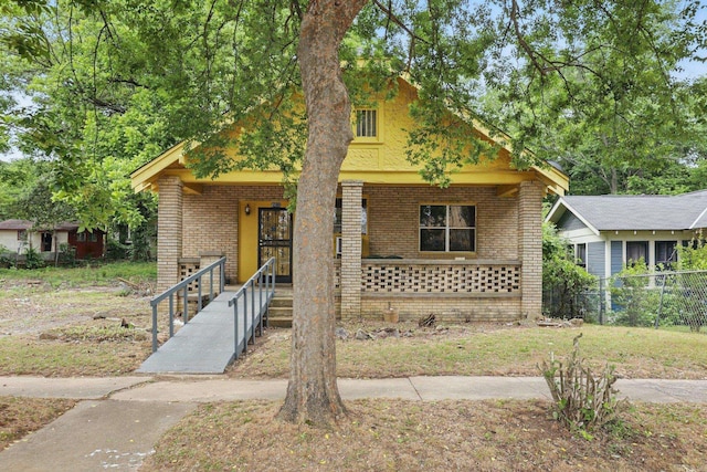 view of front of house featuring covered porch, brick siding, and fence