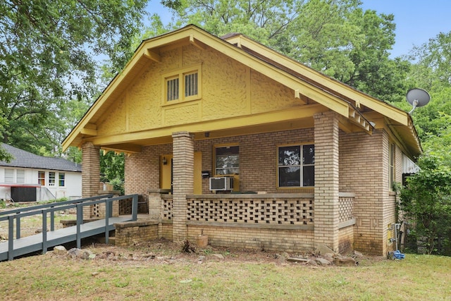 view of front of property with brick siding, covered porch, cooling unit, and a front yard