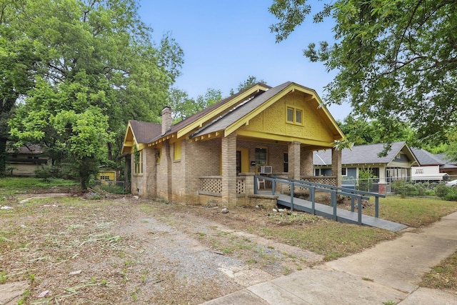 view of front facade with a porch, brick siding, a chimney, and fence