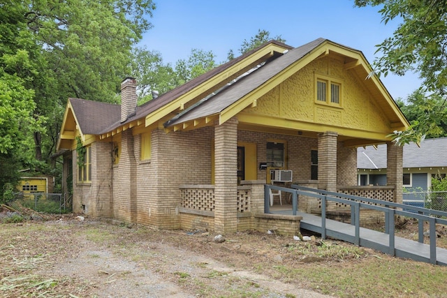 view of front of house with brick siding, fence, a chimney, and a porch