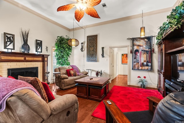 living area with a ceiling fan, a fireplace, crown molding, and wood finished floors
