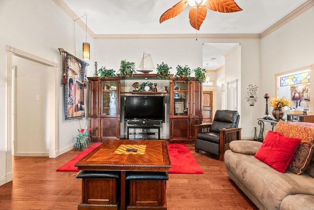 living area with ornamental molding, wood finished floors, a ceiling fan, and baseboards