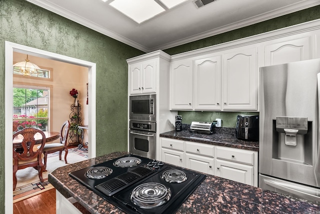 kitchen featuring appliances with stainless steel finishes, white cabinetry, wood finished floors, ornamental molding, and a textured wall