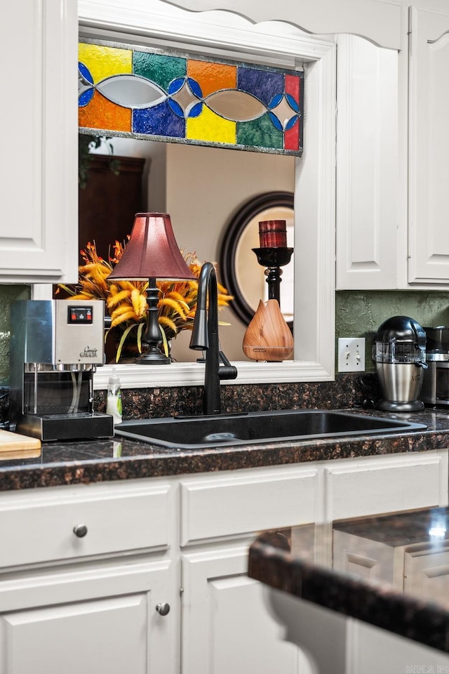 kitchen view of white cabinets, a sink, tasteful backsplash, and dark stone counters