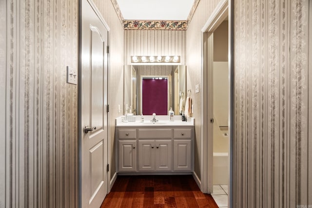 full bath featuring wallpapered walls, vanity, wood finished floors, and shower / tub combination