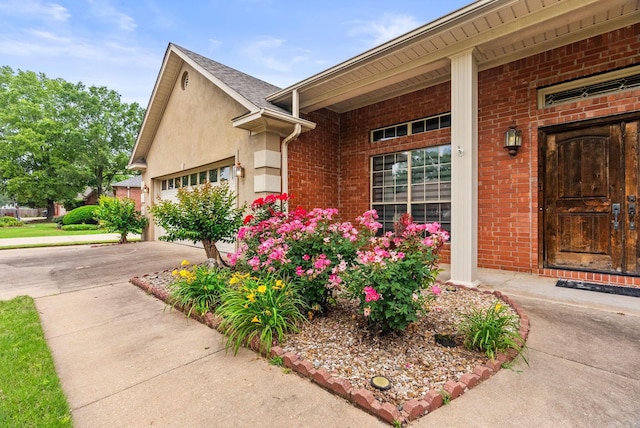 view of exterior entry featuring driveway, a garage, and brick siding