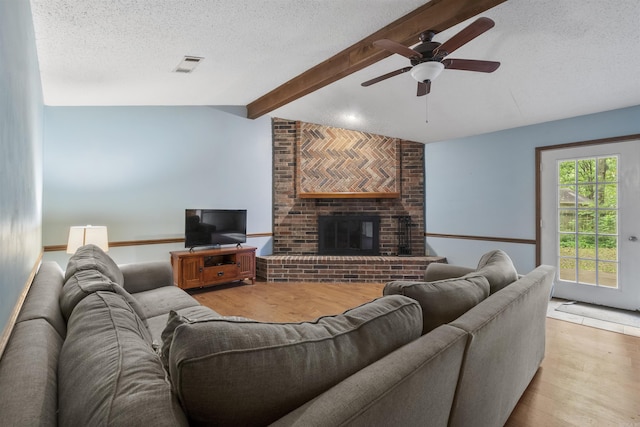 living area featuring a textured ceiling, wood finished floors, a ceiling fan, and a brick fireplace