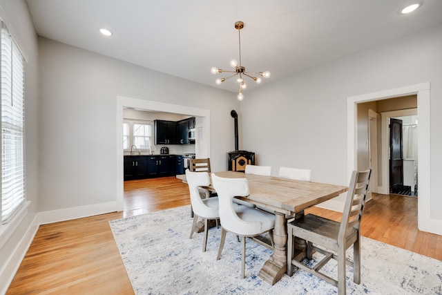 dining space with a chandelier, light wood-style flooring, baseboards, a wood stove, and recessed lighting