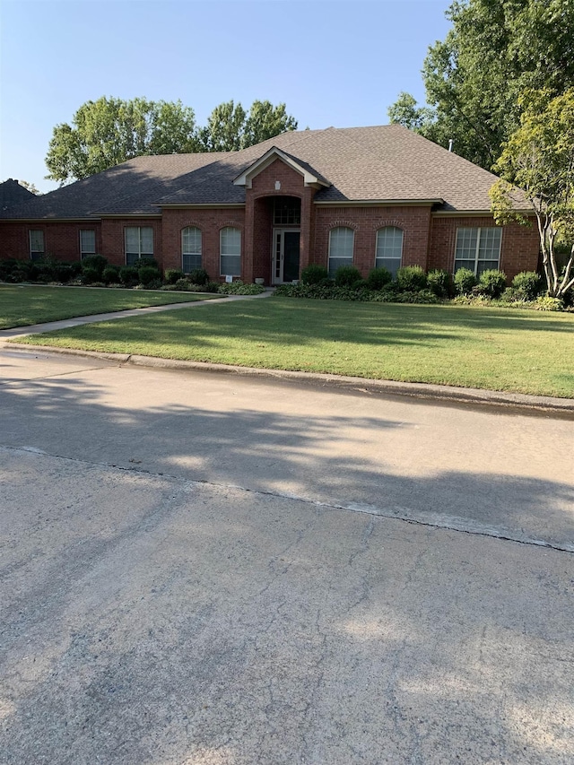 ranch-style house featuring a front lawn, brick siding, and roof with shingles