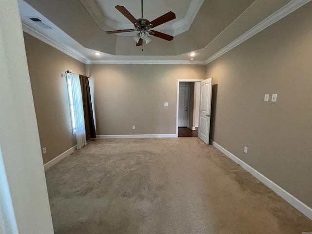 unfurnished room with a raised ceiling, ornamental molding, ceiling fan, light colored carpet, and baseboards