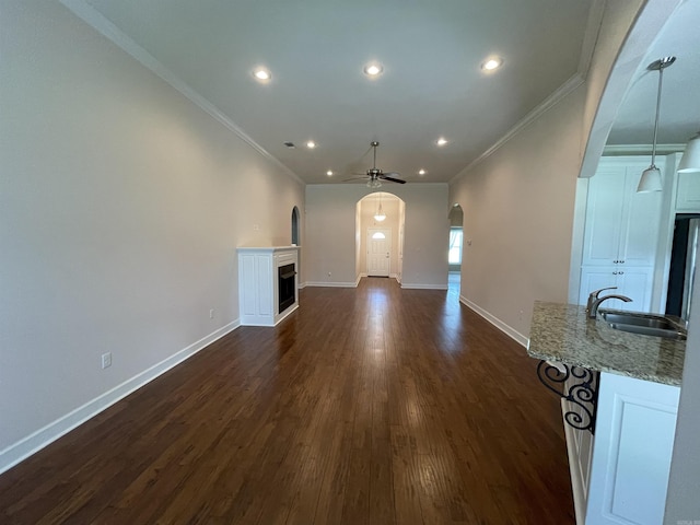 unfurnished living room featuring a sink, a fireplace, ceiling fan, ornamental molding, and arched walkways