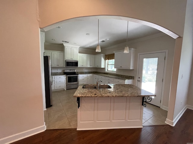 kitchen featuring appliances with stainless steel finishes, a sink, ornamental molding, arched walkways, and an island with sink