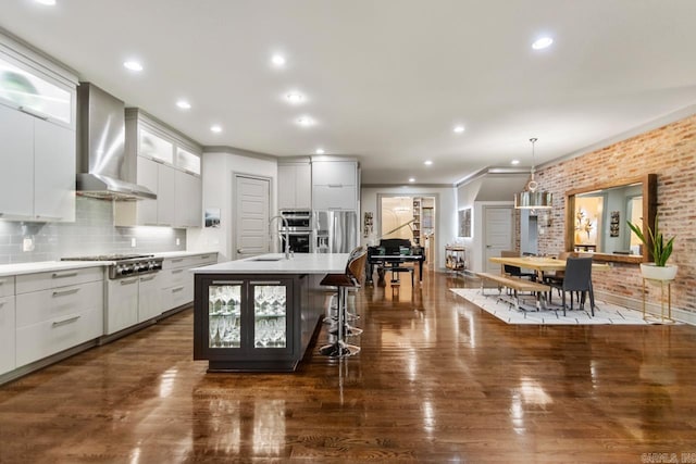 145 Cove Creek Ct, Little Rock, AR 72211 - kitchen with wall chimney range hood, ornamental molding, a kitchen island with sink, a breakfast bar, and light countertops