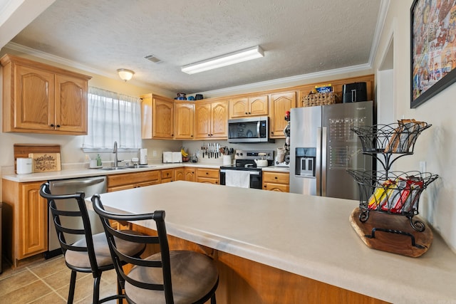 kitchen with appliances with stainless steel finishes, a sink, light countertops, a kitchen bar, and crown molding
