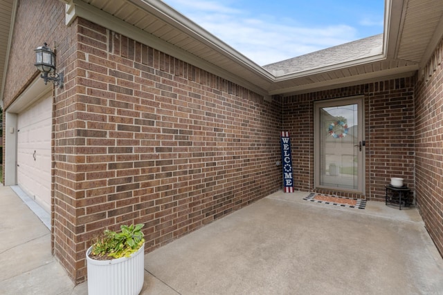 view of exterior entry with brick siding, driveway, and an attached garage