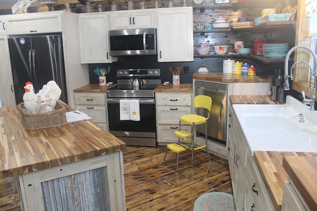 kitchen with wood counters, appliances with stainless steel finishes, a sink, dark wood finished floors, and white cabinets