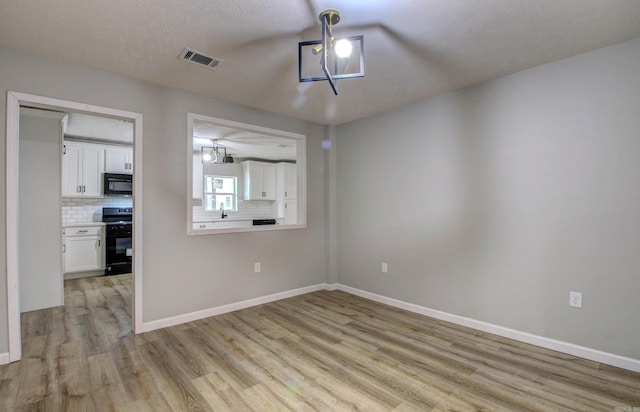 spare room featuring light wood-style flooring, baseboards, a sink, and a textured ceiling