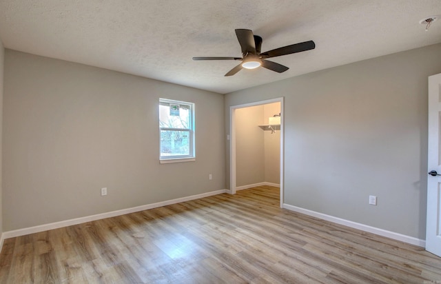 unfurnished bedroom featuring wood finished floors, baseboards, a spacious closet, and a textured ceiling