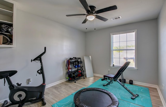 exercise room with light wood finished floors, a ceiling fan, and baseboards