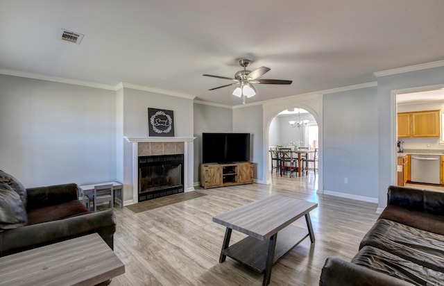 living area featuring arched walkways, a ceiling fan, light wood-style flooring, a chandelier, and crown molding