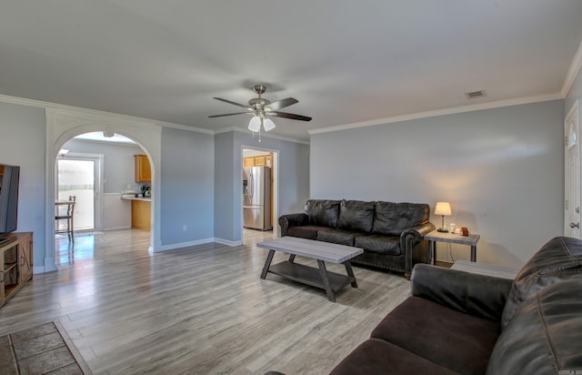 living room featuring arched walkways, ceiling fan, light wood-style floors, ornamental molding, and baseboards