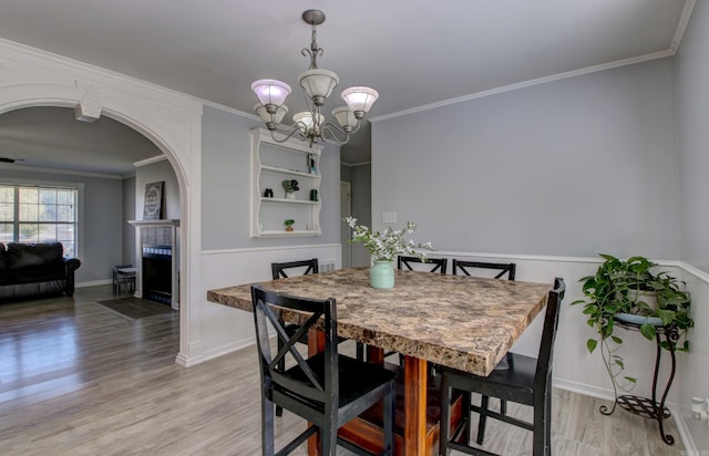 dining room featuring light wood-style flooring, arched walkways, a fireplace, a chandelier, and wainscoting