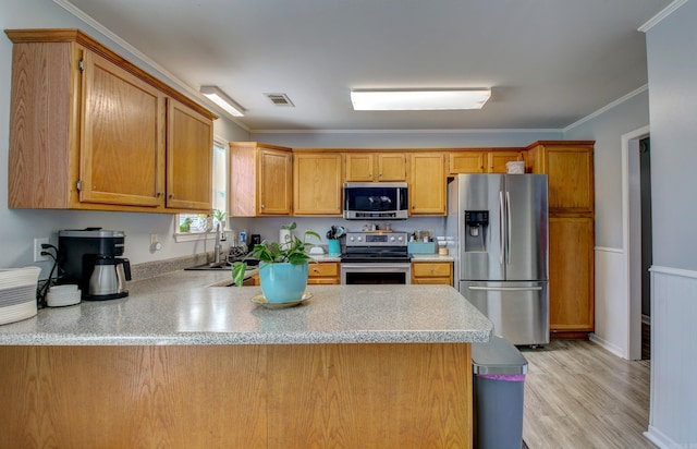 kitchen featuring appliances with stainless steel finishes, a peninsula, a sink, light wood finished floors, and crown molding