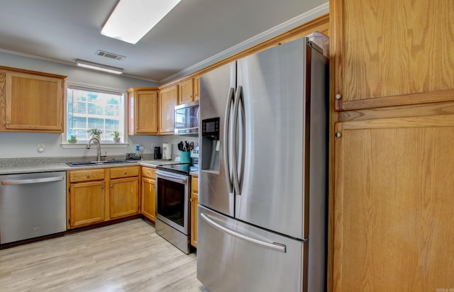 kitchen with stainless steel appliances, a sink, ornamental molding, light wood-style flooring, and light countertops