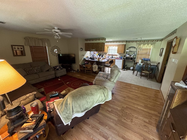 living area featuring a textured ceiling, ceiling fan, and light wood-type flooring