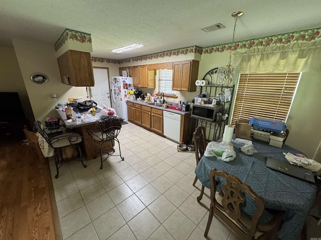 kitchen featuring white appliances, a sink, a textured ceiling, light tile patterned floors, and brown cabinetry
