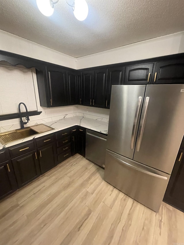 11808 Saint Charles Blvd, Little Rock, AR 72211 - kitchen with stainless steel appliances, dark cabinetry, a sink, light wood finished floors, and a textured ceiling
