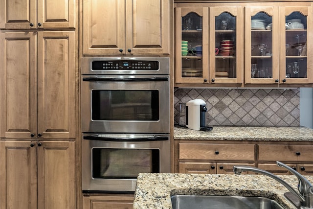 110 Clervaux Cir, Little Rock, AR 72223 - kitchen with double oven, a sink, backsplash, light stone countertops, and glass insert cabinets