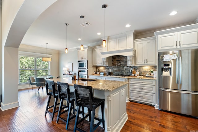 43 Tournay Cir, Little Rock, AR 72223 - kitchen featuring appliances with stainless steel finishes, decorative backsplash, dark wood finished floors, a kitchen island with sink, and light stone countertops