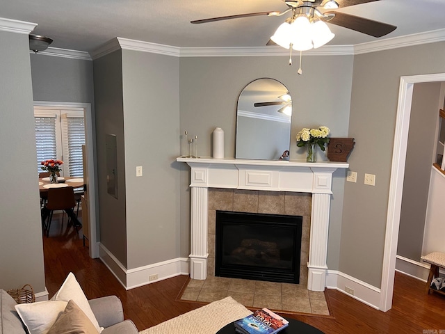 living area featuring wood finished floors, ceiling fan, crown molding, a tile fireplace, and baseboards