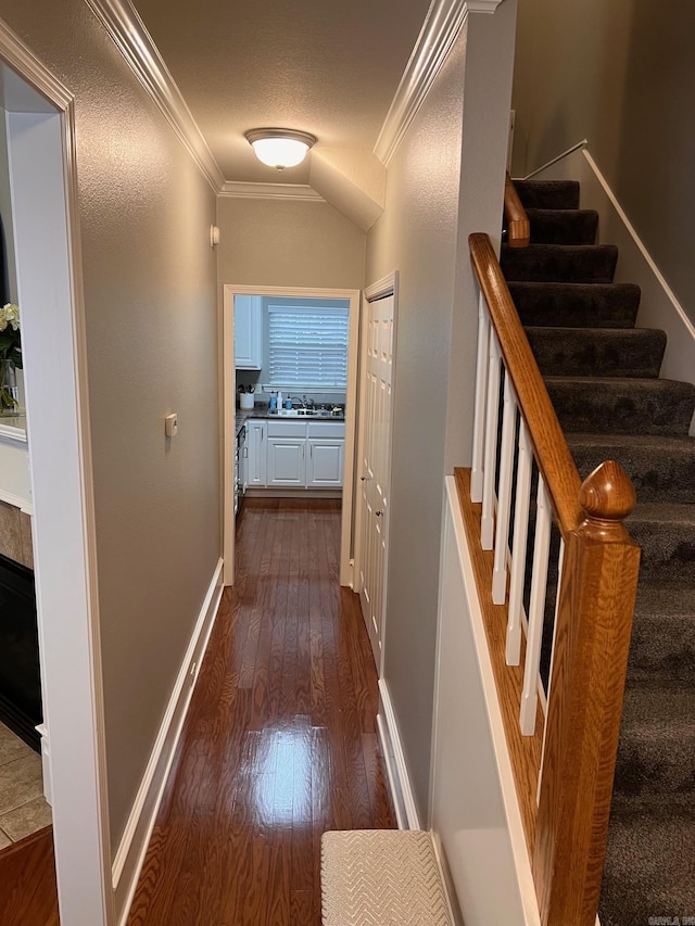 corridor with ornamental molding, dark wood-type flooring, stairway, a sink, and baseboards