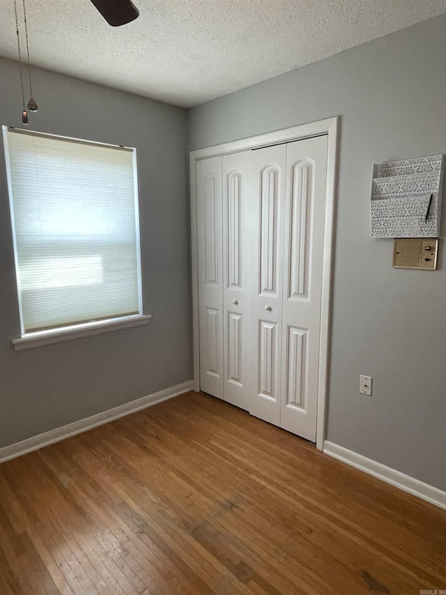 unfurnished bedroom with wood finished floors, a closet, a textured ceiling, baseboards, and a ceiling fan