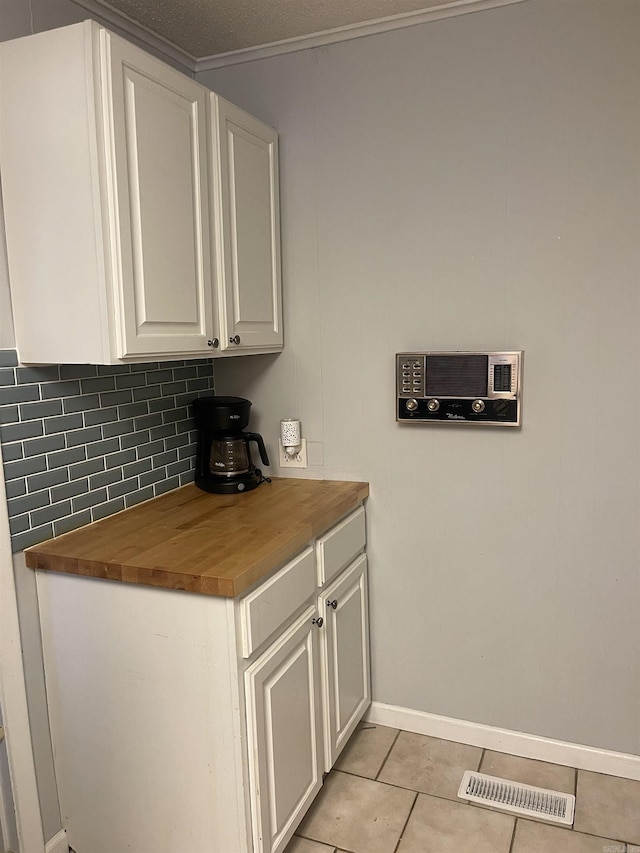 kitchen featuring butcher block counters, white cabinets, backsplash, light tile patterned floors, and ornamental molding