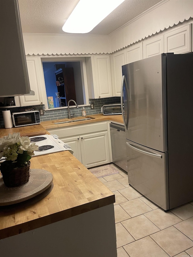 kitchen featuring stainless steel appliances, butcher block counters, a sink, backsplash, and a textured ceiling