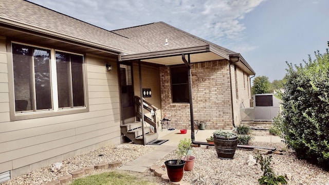 view of exterior entry with brick siding and a shingled roof