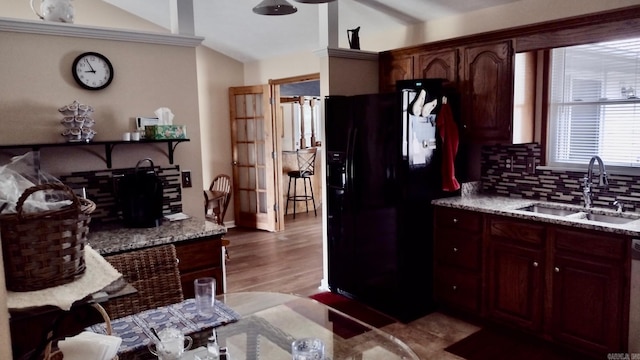 kitchen with black fridge, a sink, backsplash, light wood-type flooring, and light stone countertops