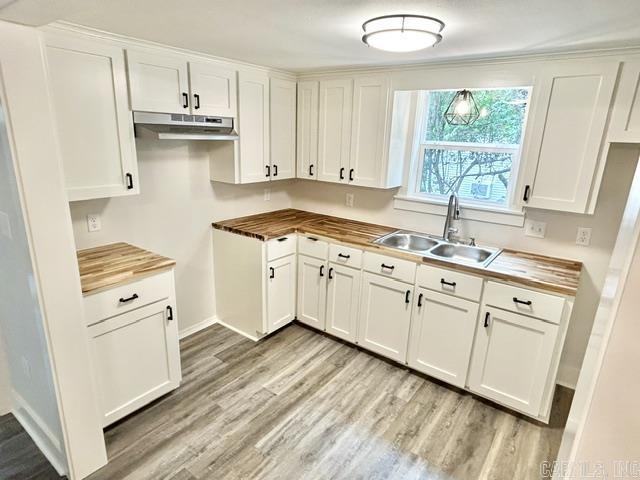 1307 Aplin Ave, Perryville, AR 72126 - kitchen featuring butcher block countertops, under cabinet range hood, a sink, light wood-style flooring, and white cabinets