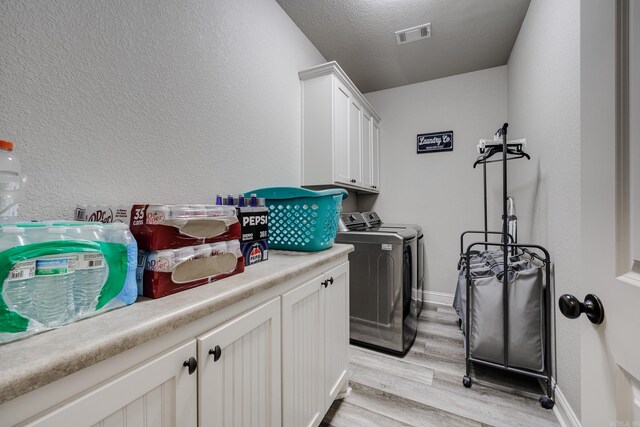 1715 Sylar Cir, Conway, AR 72034 - laundry area featuring washing machine and clothes dryer, light wood-style flooring, cabinet space, baseboards, and a textured wall