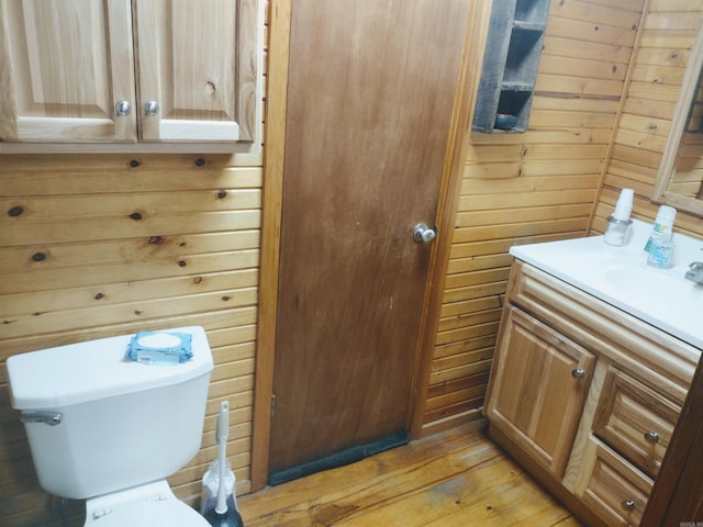 bathroom with wood-type flooring, vanity, toilet, and wood walls