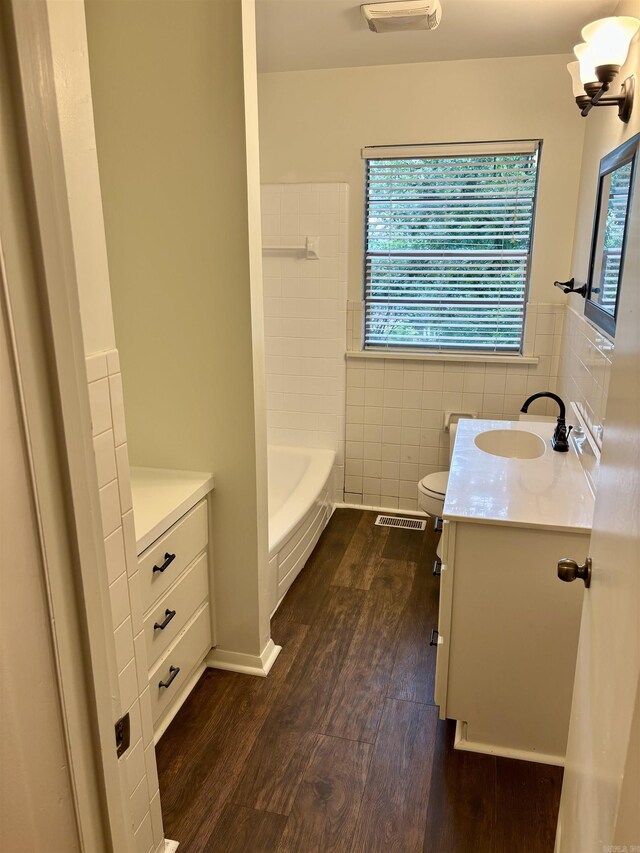 704 W 56th St, North Little Rock, AR 72118 - bathroom with wood finished floors, vanity, tile walls, toilet, and a wainscoted wall