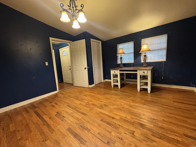 unfurnished office featuring lofted ceiling, wood finished floors, a chandelier, and baseboards