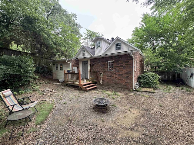 rear view of house with a wooden deck, an outdoor fire pit, brick siding, and a fenced backyard