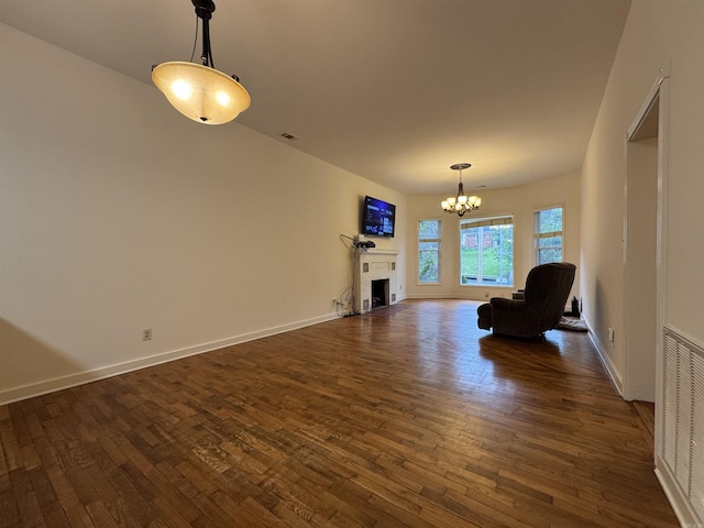 unfurnished living room with dark wood-style flooring, a chandelier, a fireplace, and baseboards