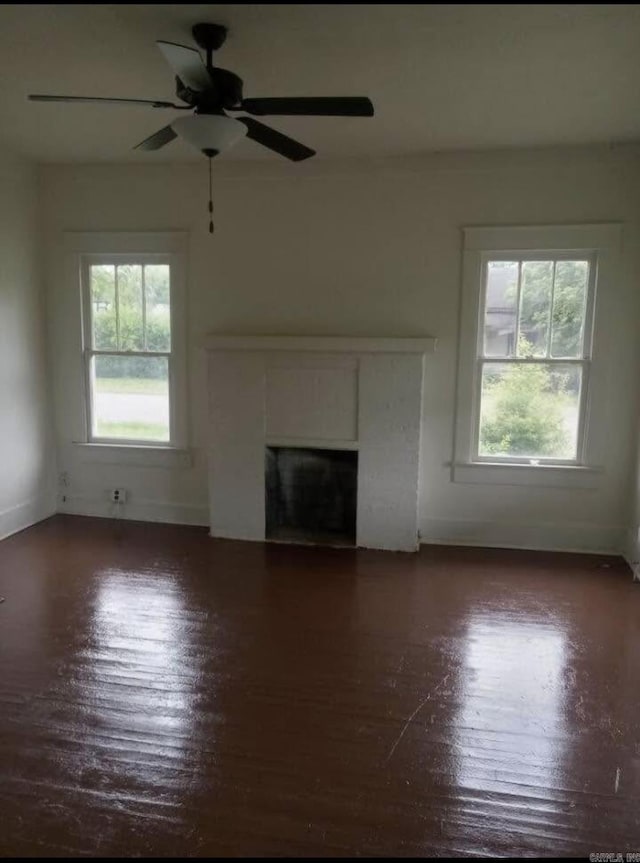 1700 Moss St, North Little Rock, AR 72114 - unfurnished living room featuring healthy amount of natural light, dark wood-style floors, a fireplace with flush hearth, and a ceiling fan
